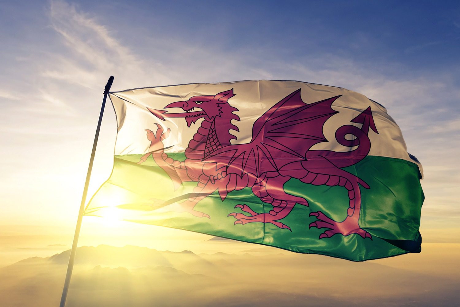 Welsh flag - green and white background with a big red dragon on the front - waving in front of a sunset.